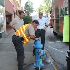Randy Olson, white shirt, background, oversees a hydrant test downtown before the Sooie't Relief BBQ Benefit.
 
 