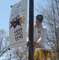 Michael Paulson attaches a banner to a light post on Randall Street announcing the coming Greer Family Fest.
 