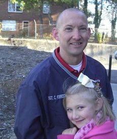 Maddie Forrester, 7, cozies up to her father, Sgt. Chris Forrester of the Greer Police Department, for warmth in the cold, windy weather this morning at the Cannon Centre. Maddie accompanied her father to the Cops for Tots distribution. 