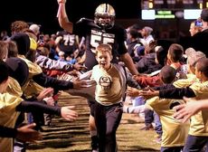 Brody Young, 12, leads Kameron Laue (55) through a gauntlet of youth football players at Dooley Field on Friday night. Brody is the son of coach Will Young.