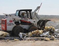 A bobcat is used to move debris in a pile.