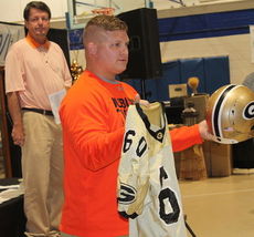 Robbie Gravely, background, the voice of the Greer Yellow Jackets Sports Network, glances over at Noah Hannon during the live auction for his jersey and a Greer football helmet.
 