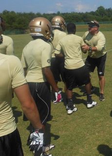 Greer Athletics Director Travis Perry halts his players from getting onto the field during a free-for-all midway during today's passing scrimmage with Greenville. Perry didn't get out unscathed as he received kicks and scrapes on his legs.