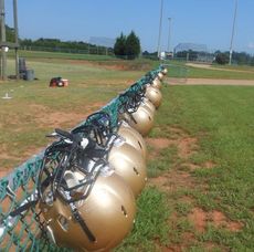 Gold helmets line the Greer practice field fence to symbolize players being prohibited from wearing helmets and shoulder pads during the first days of summer practice.