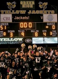 Greer players celebrate their perfect regular season in front of the scoreboard.
 