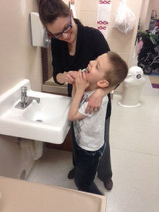 Washington Center at Hollis student Evan Nivens brushes his teeth after breakfast, with some help from Para-Educator Aly Malone.