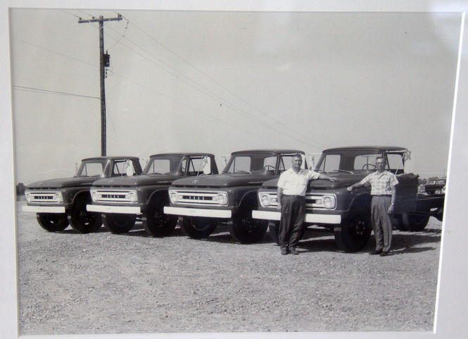 Daniel and an unidentified person stand near a row of Ford Trucks.