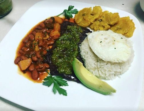 On the home page: Bandeja de Isla or (island tray) consists of a skirt steak topped with house-made sofrito vinaigrette, arroz blanco y habichuelas, tostones, slice of avocado, and topped with a fried egg.
 