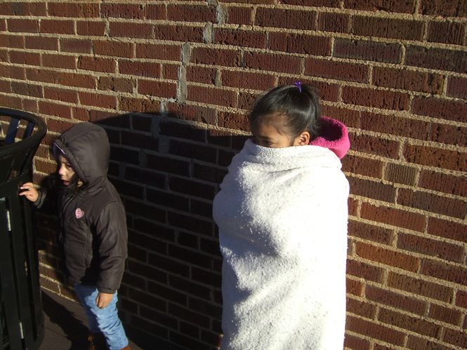 Alexander Chabarria huddles in a blanket against an outside wall at the Cannon Centre this morning as she waits in line for the distribution of toys by the Greer Police Department's Cops for Tots program.